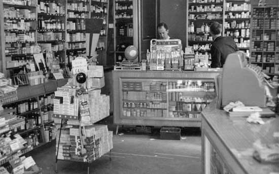 Michaels pharmacy interior in the 1950s with a young Alan Michael behind the counter.